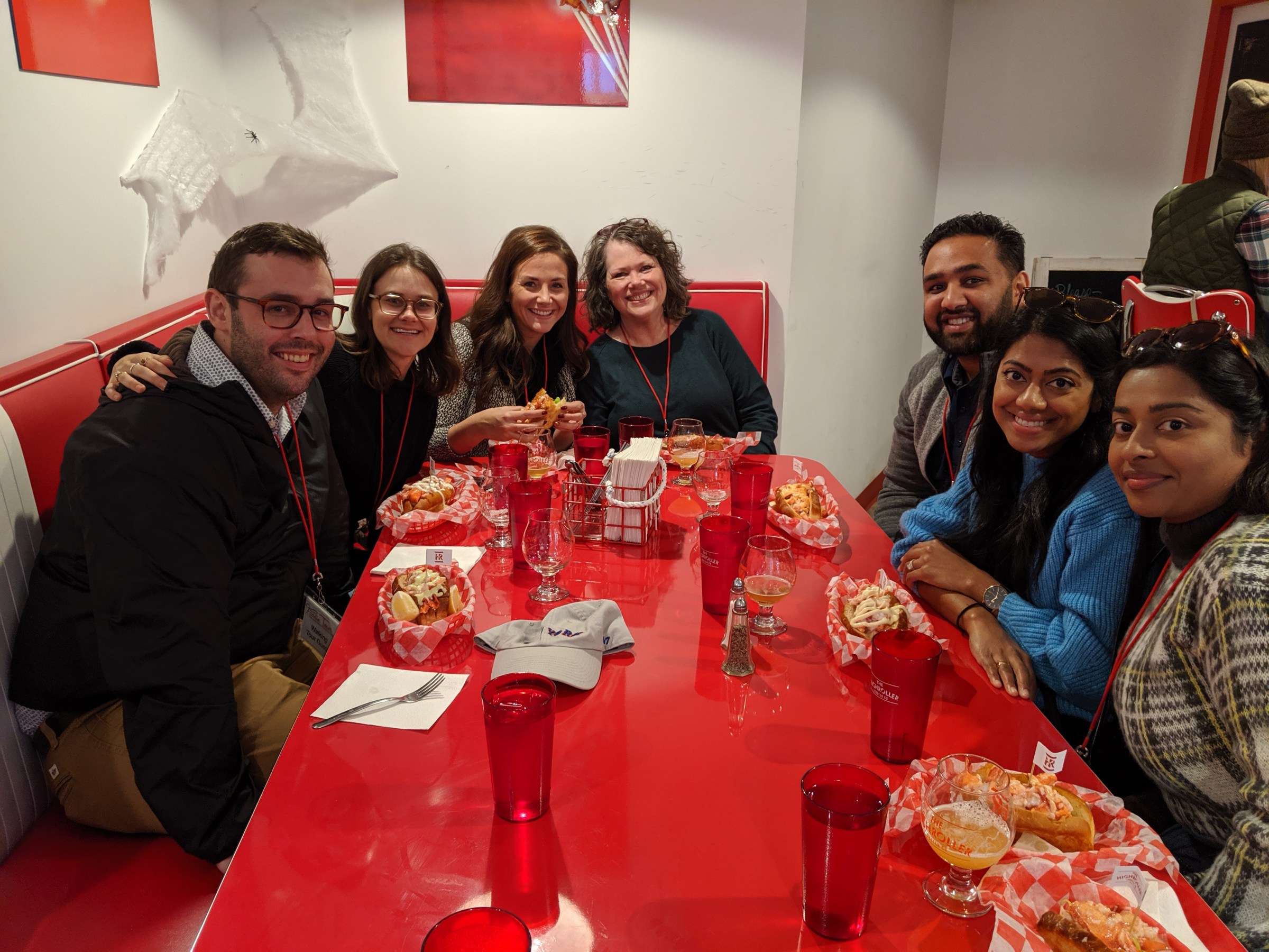 a group of people sitting at a table eating lobster rolls