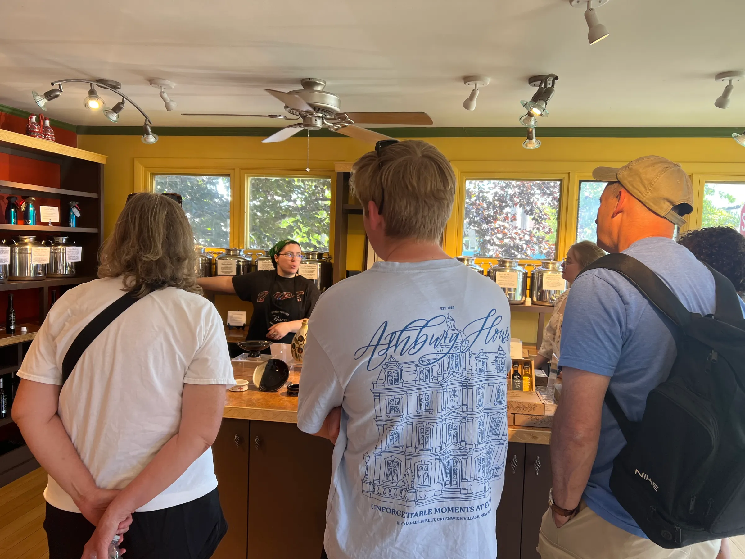 People gather around a counter in a coffee shop, listening to a barista.