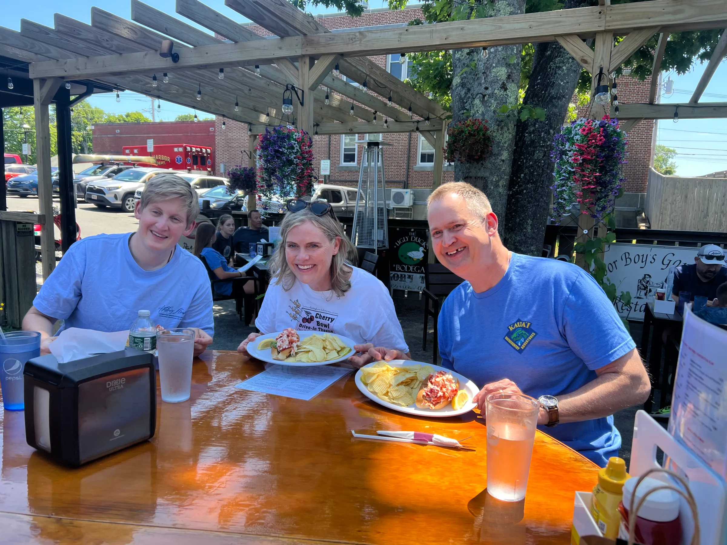 Three people smiling at an outdoor restaurant table with food.