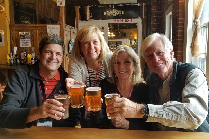 Four people smiling, holding beer glasses in a bar setting.