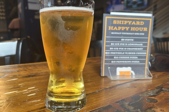 Glass of beer on wooden table near a happy hour sign.