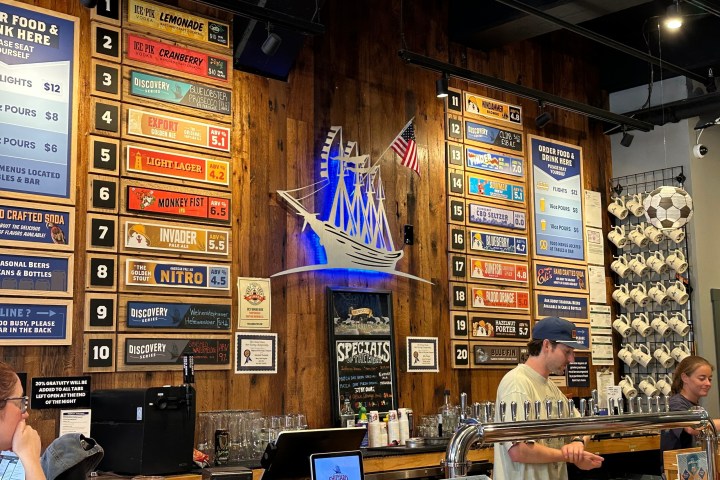 Bar with wooden wall, beer menu, large ship decoration, and patrons ordering drinks.