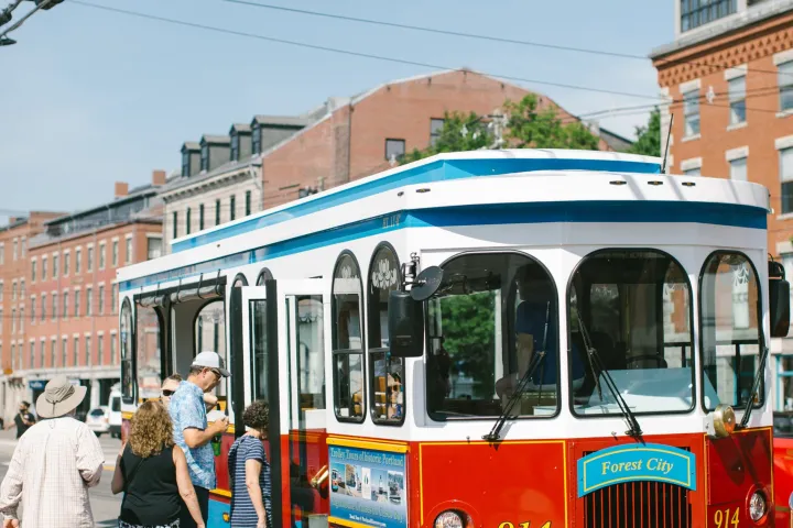 People boarding a blue and red trolley on a brick-paved street.
