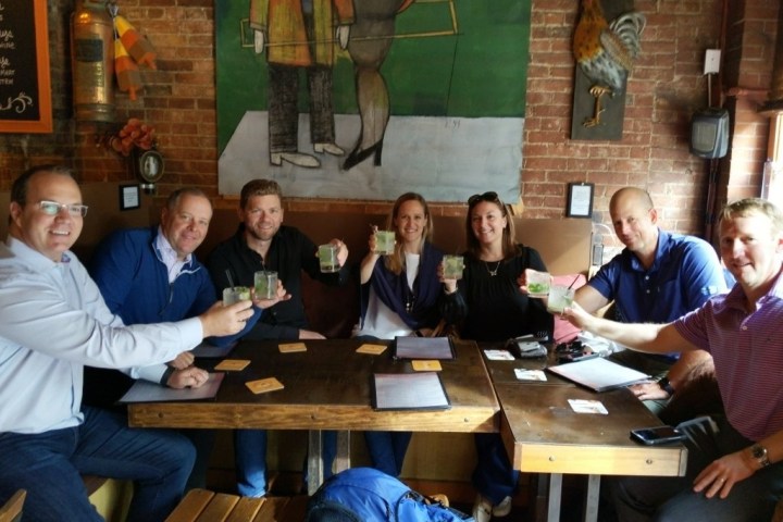 Group of seven people seated at a table, holding drinks in a cafe.