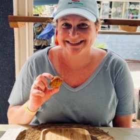 Person smiling, holding a small food item at a table with a wooden plate.