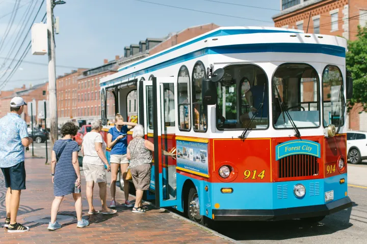 People boarding a red and blue trolley bus on a city street.
