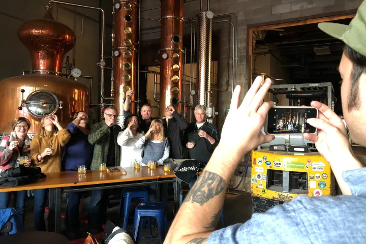 Group of people posing for a photo inside a distillery with large copper equipment.