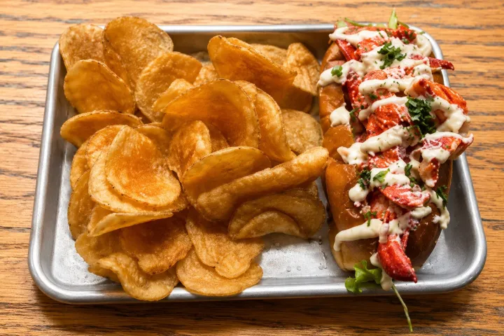 Lobster roll with sauce and parsley, served with potato chips on a tray.