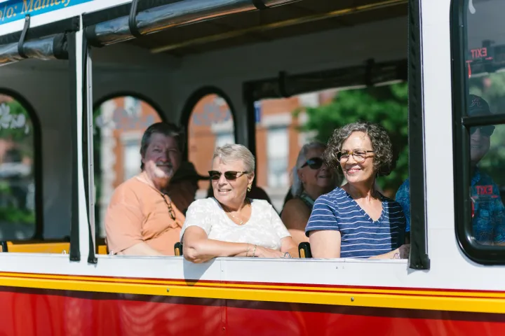Smiling group on a red and white open-air bus.