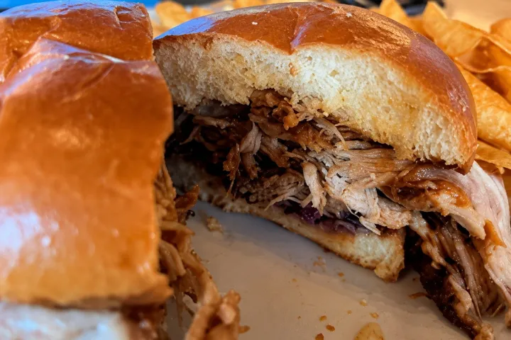 Pulled pork sandwich with crispy chips in the background.